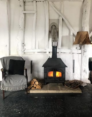 Log burner alight next to a chair with grey throw rug over it